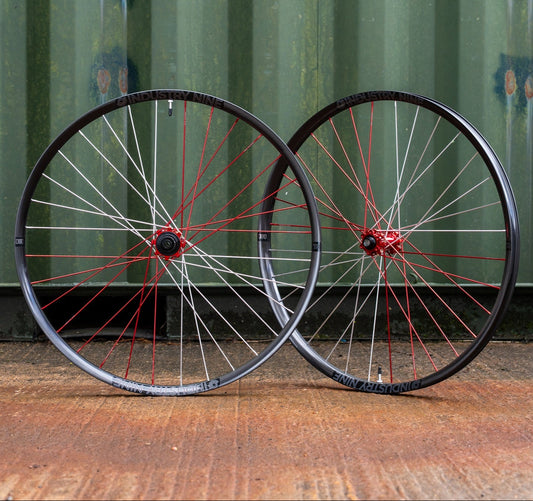 Two bicycle wheels with red spokes on a wooden surface against a green metal container background.